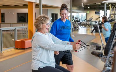An Aims personal trainer helping a person to use exercise equipment at the PERC