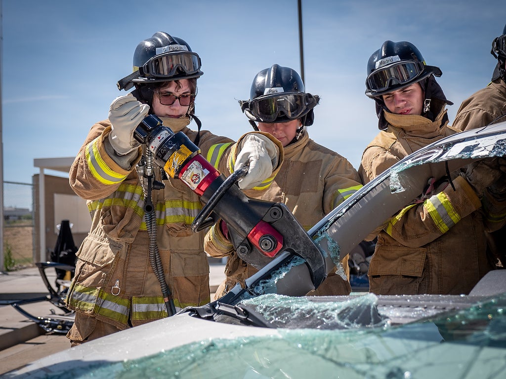 Aims fire science Xplore Academy students practicing using jaws of life equipment on a vehicle