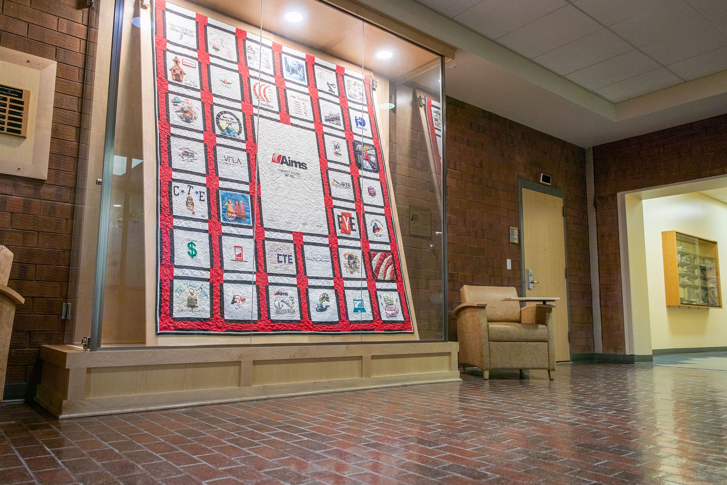 A display case holding a memory quilt featuring the history of Aims Community College.