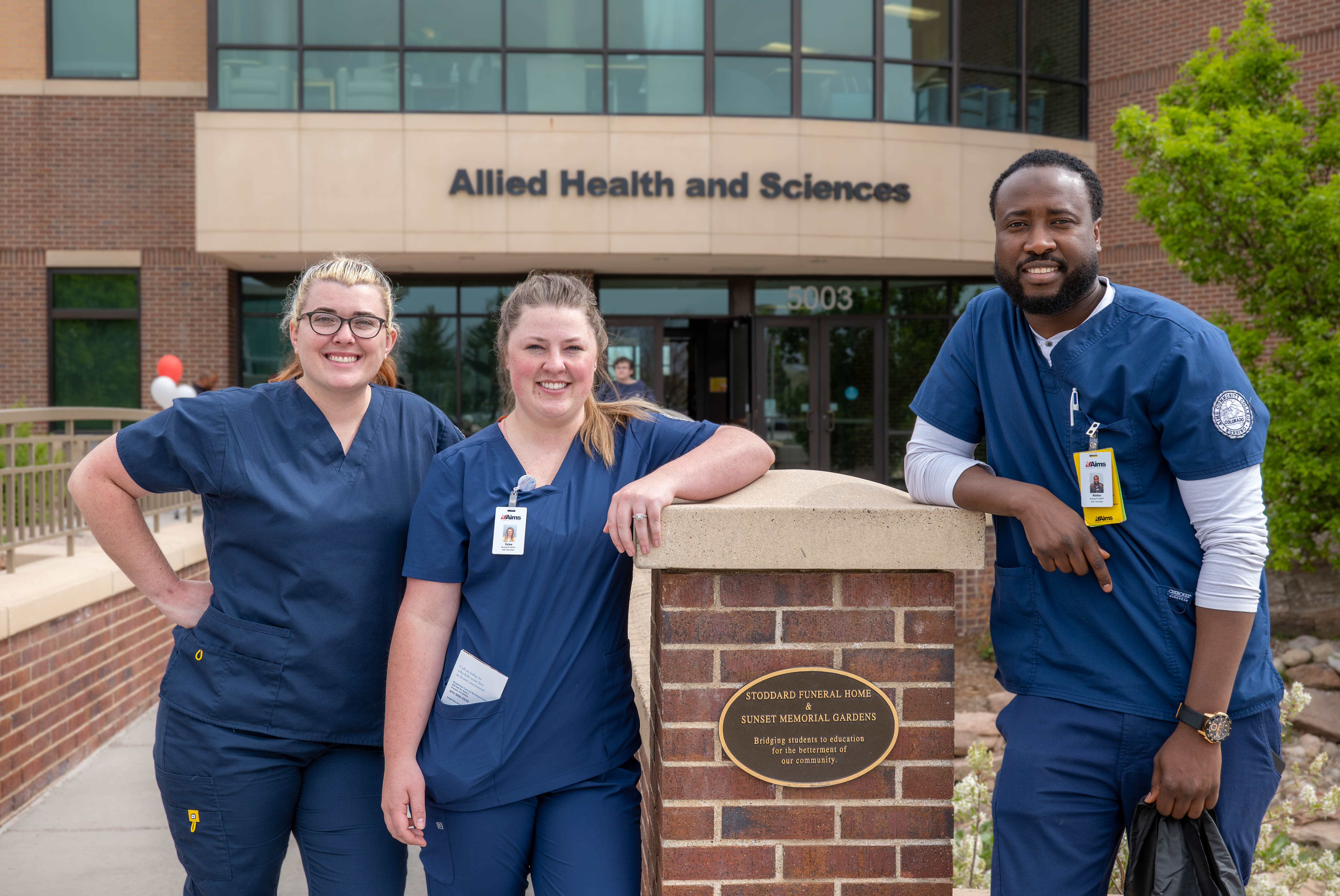Three nursing students stand outside of the Allied Health and Sciences building.