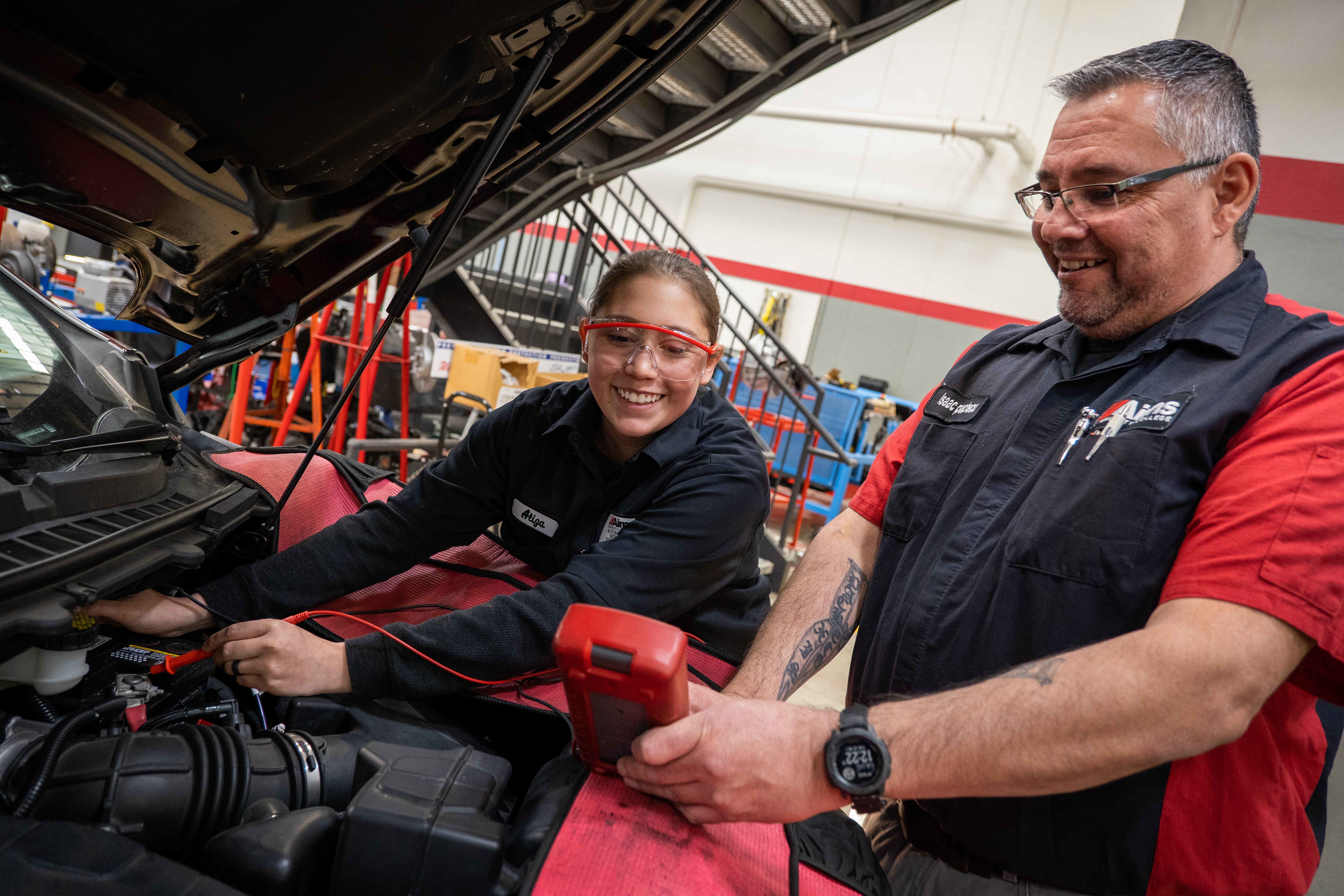 An automotive student is working on a car with her instructor helping.