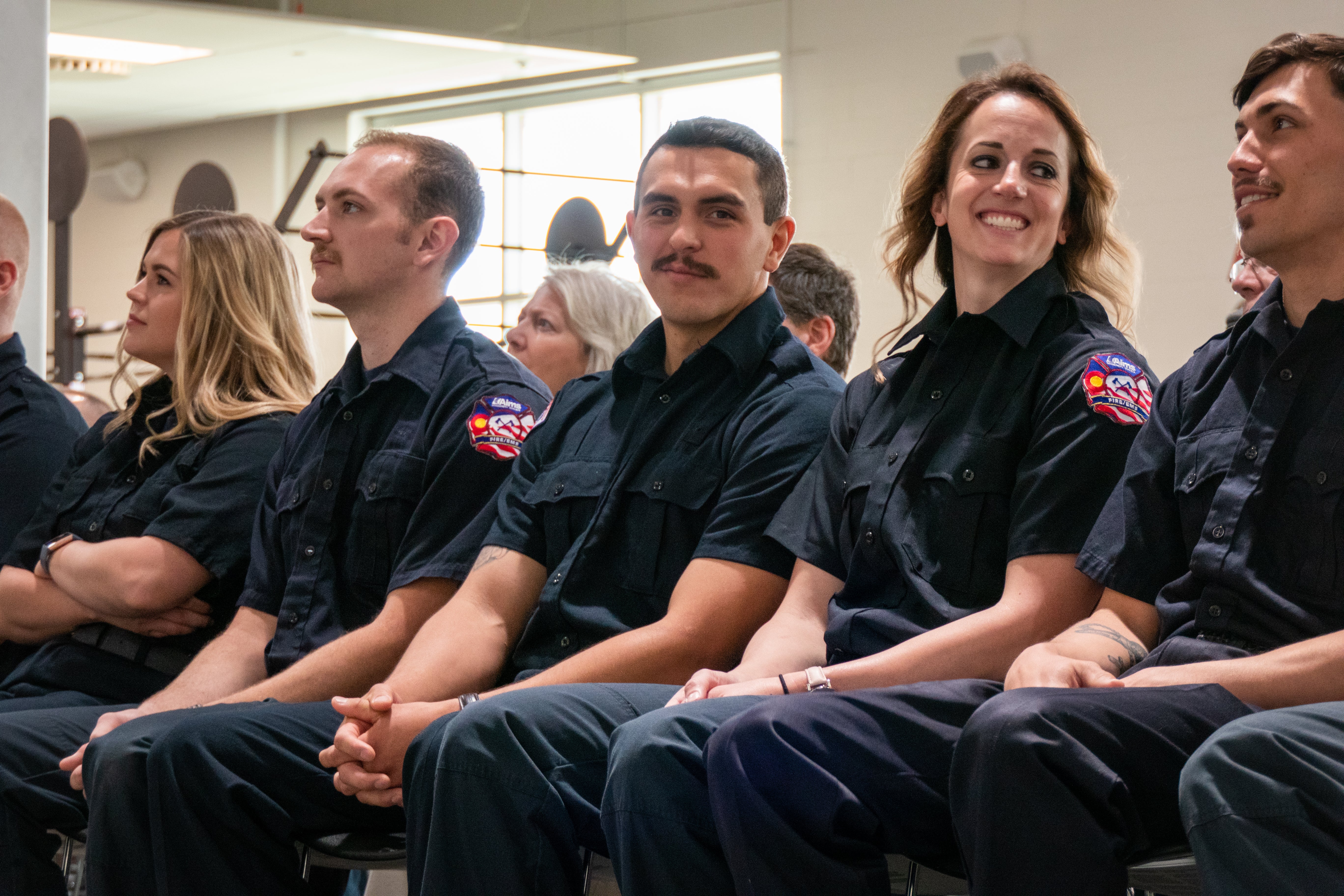 A row of fire academy students are seated together with their navy jumpsuits.