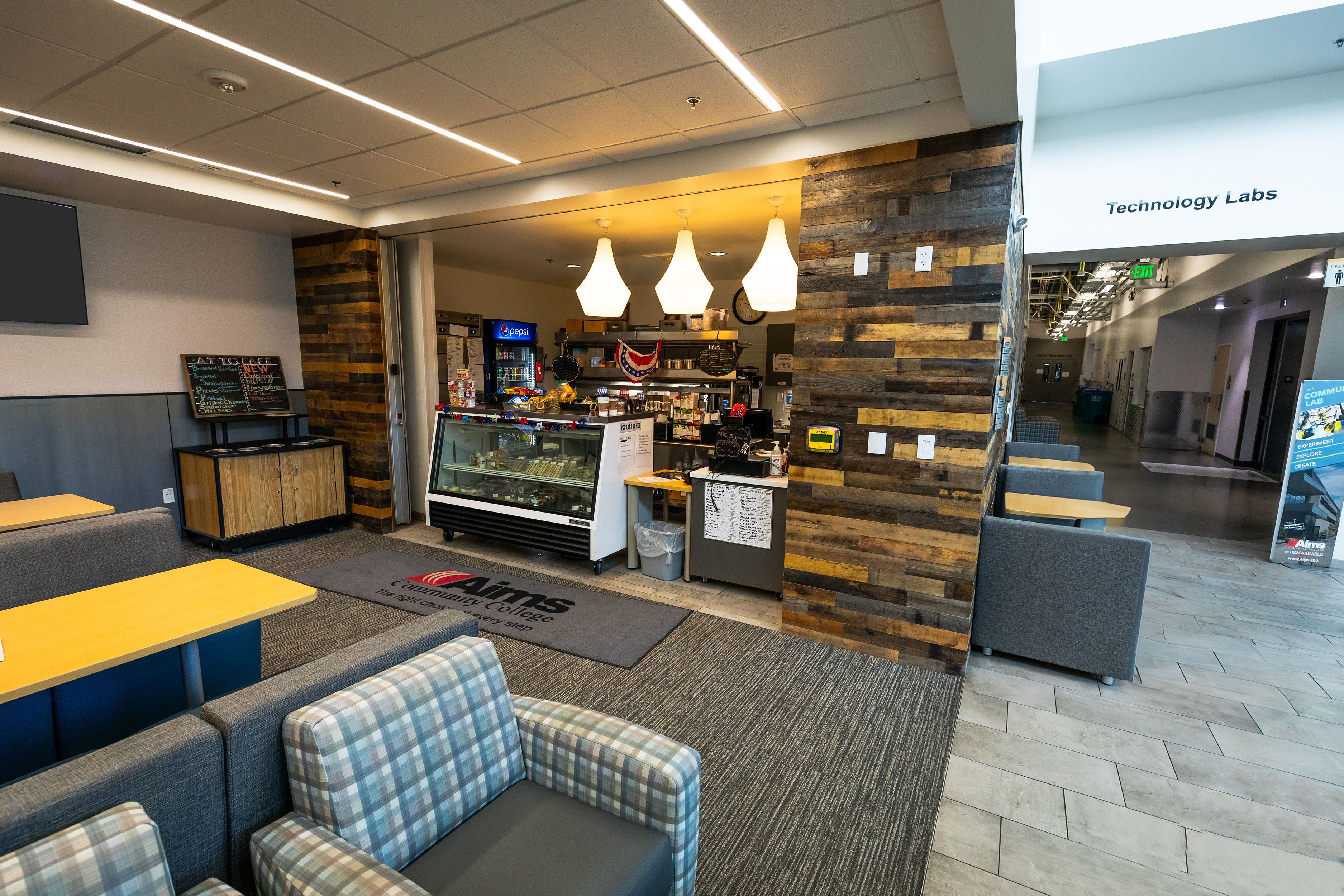 Exterior of Arty's Cafe. A cash register next to a cold food display. Chairs and tables are nearby for use.