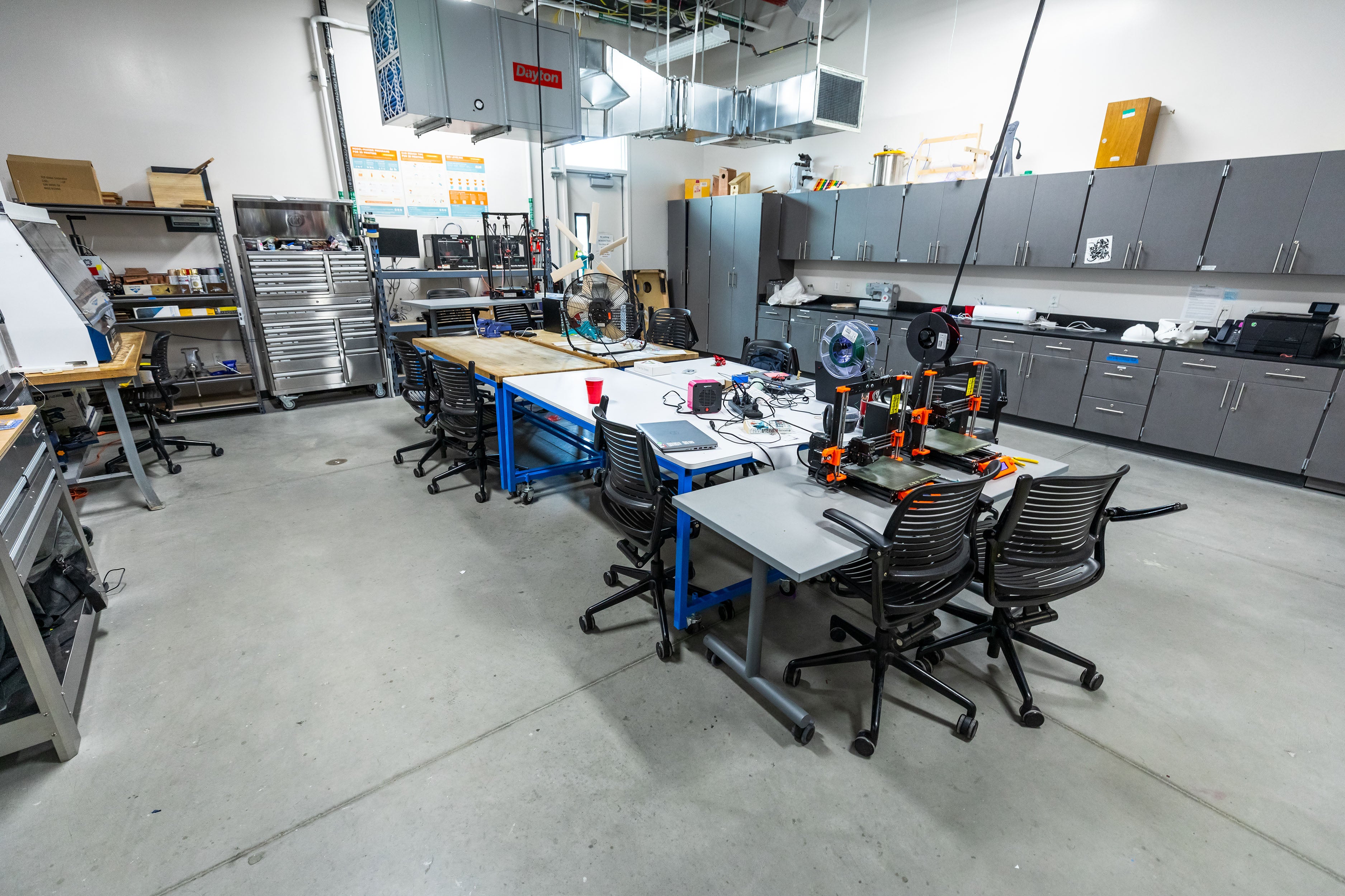 Interior photo of the Community Lab. A large central work area with 3D printers and workstations.