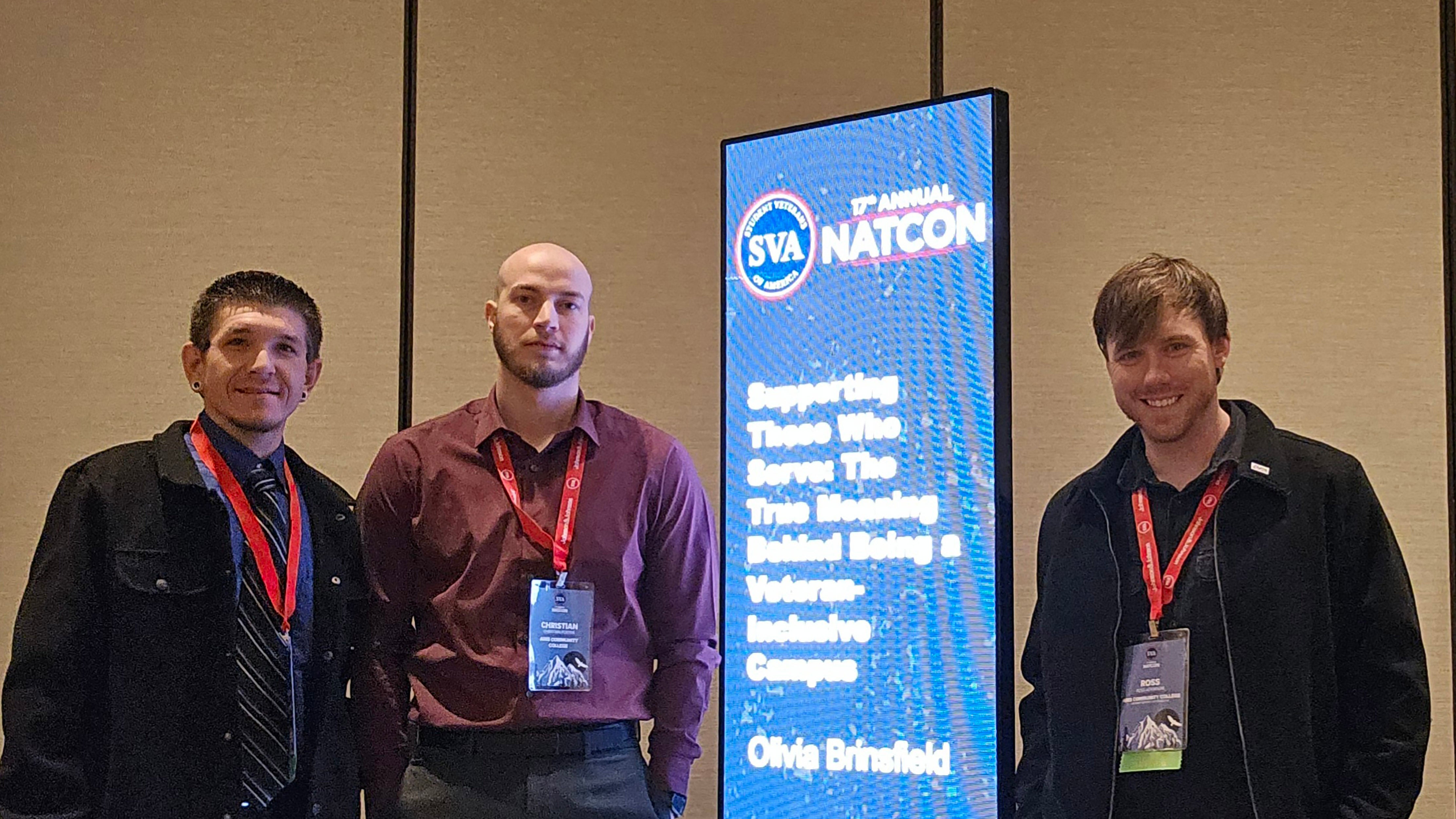 3 men standing next to blue banner with white text that reads &quot;17th Annual NATCON Supporting those who serve the true meaning behind being a veteran inclusive campus&quot;