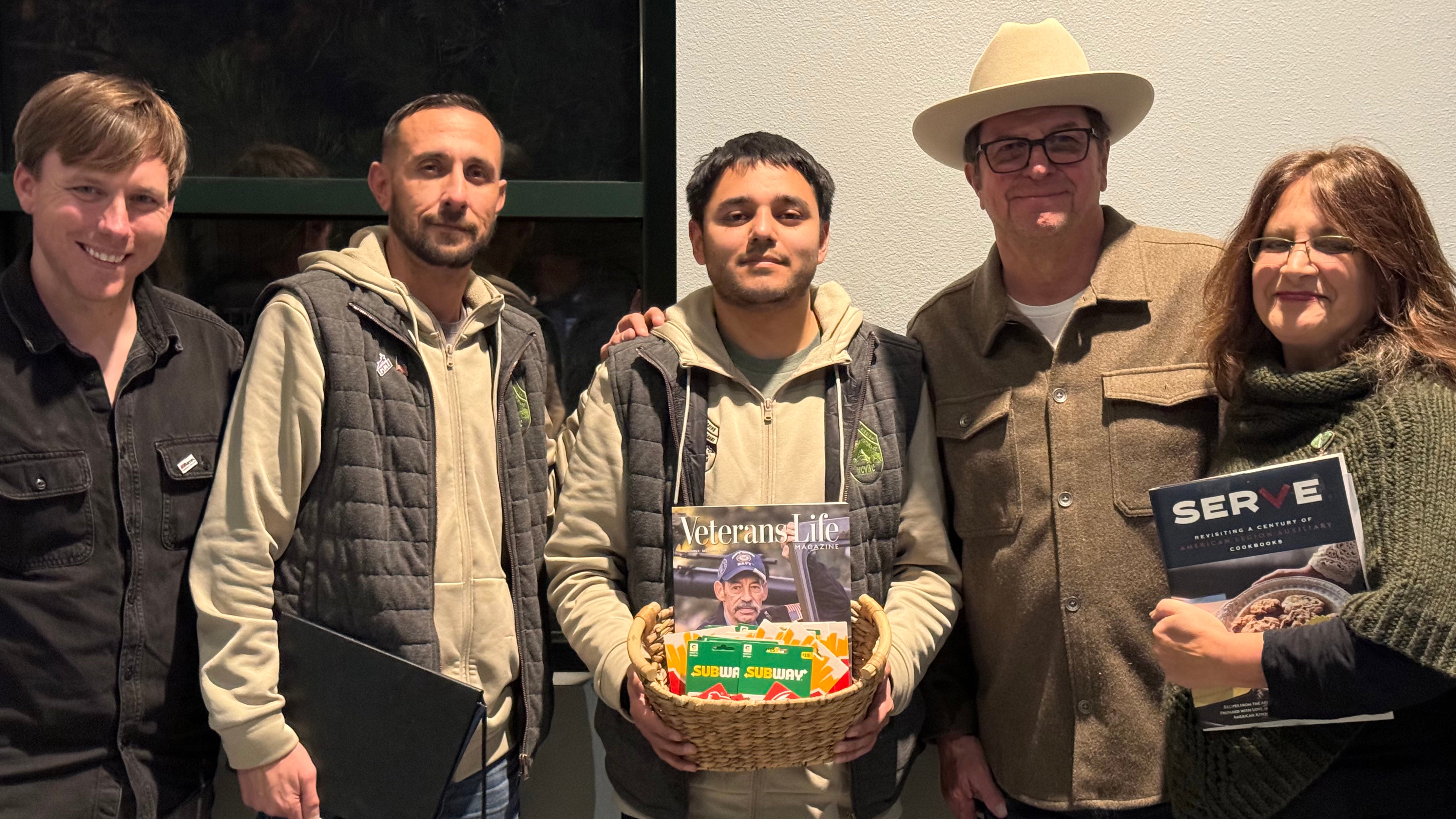 5 veterans standing side by side one in center holding a basket with books