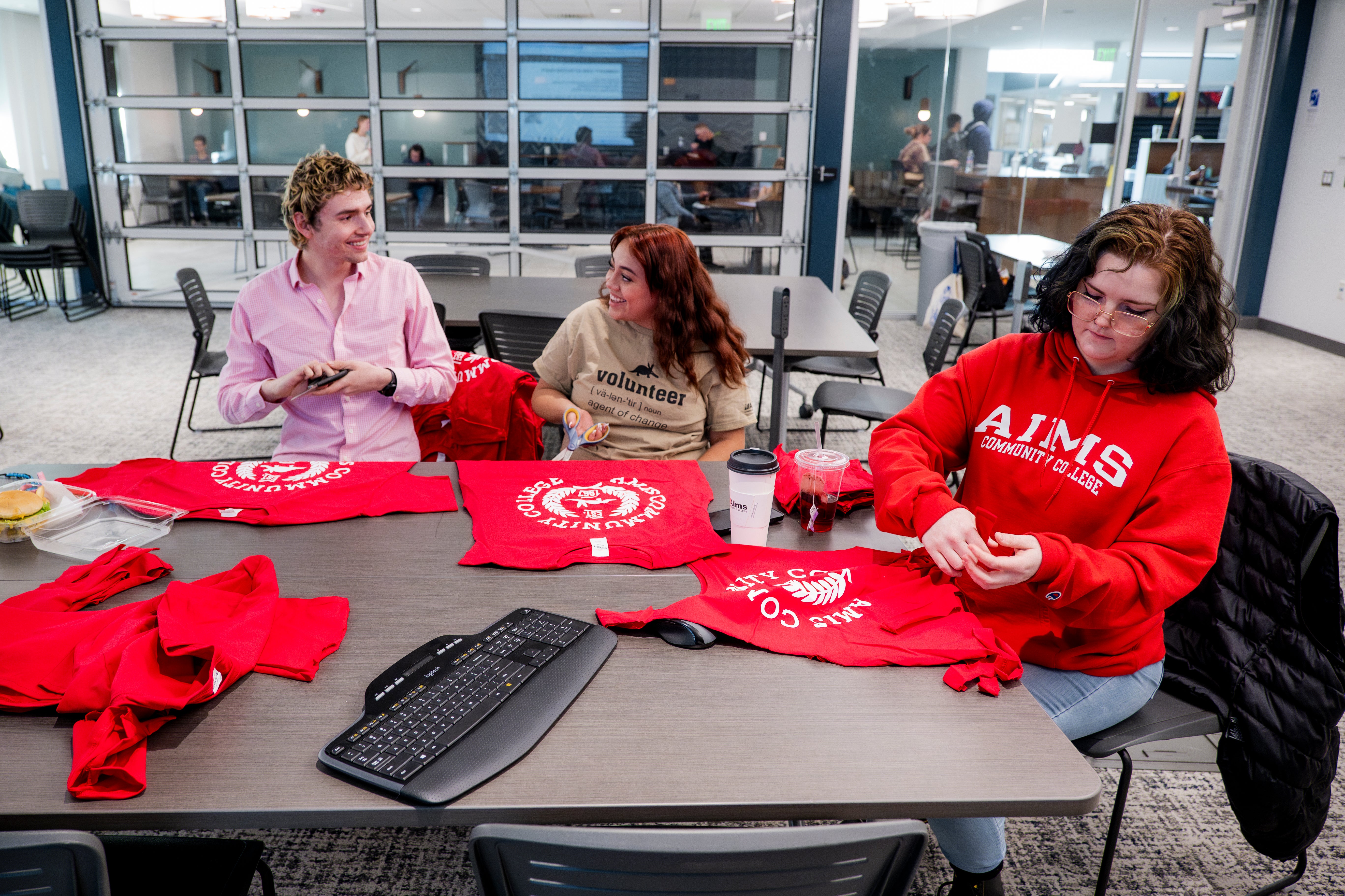 Three students sit at a table packaging red Aims shirts for the community care packages.