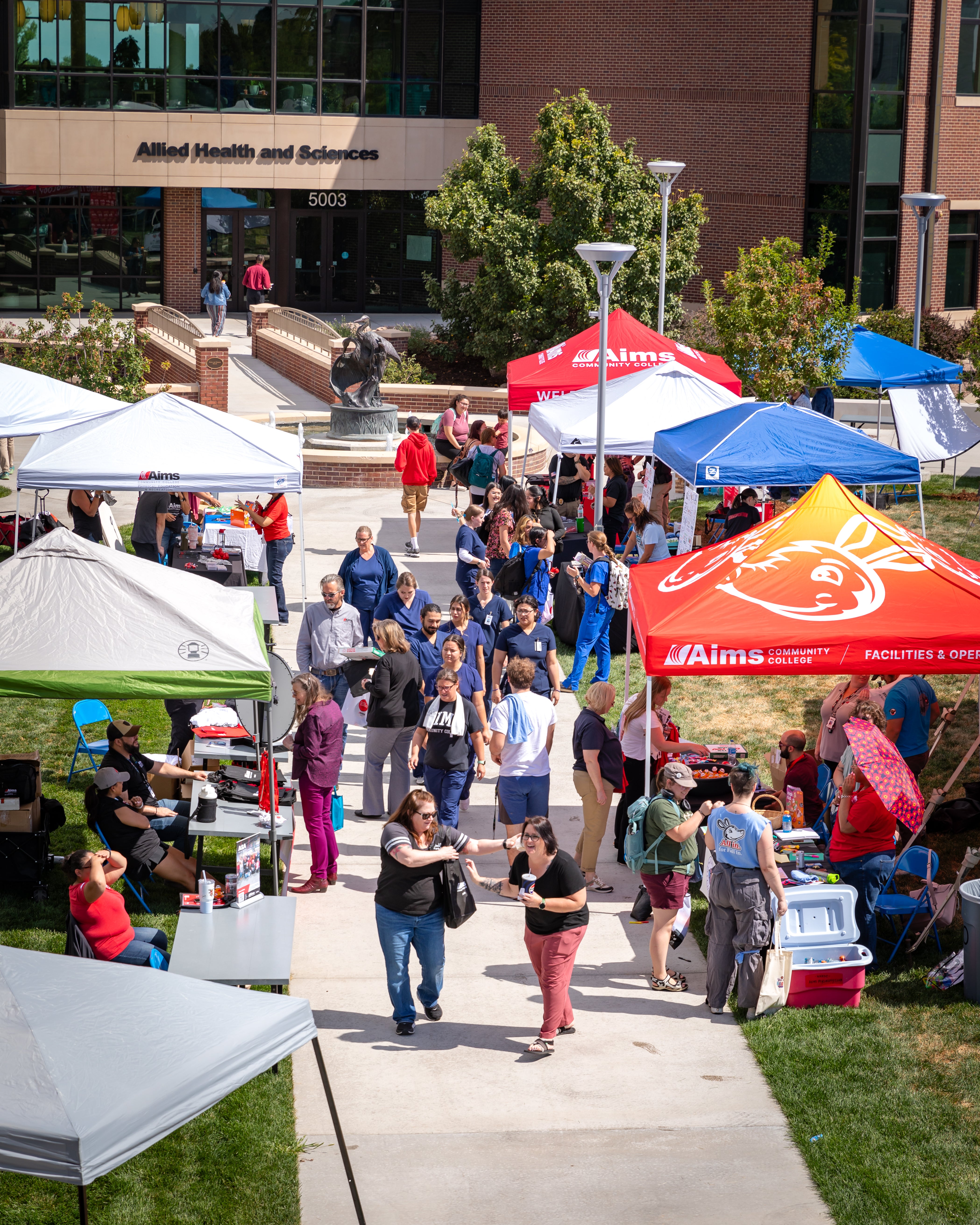 An overhead view of small tents set up outside the Allied Health building. Students are wandering amongst the tents learning about different Aims services and clubs.