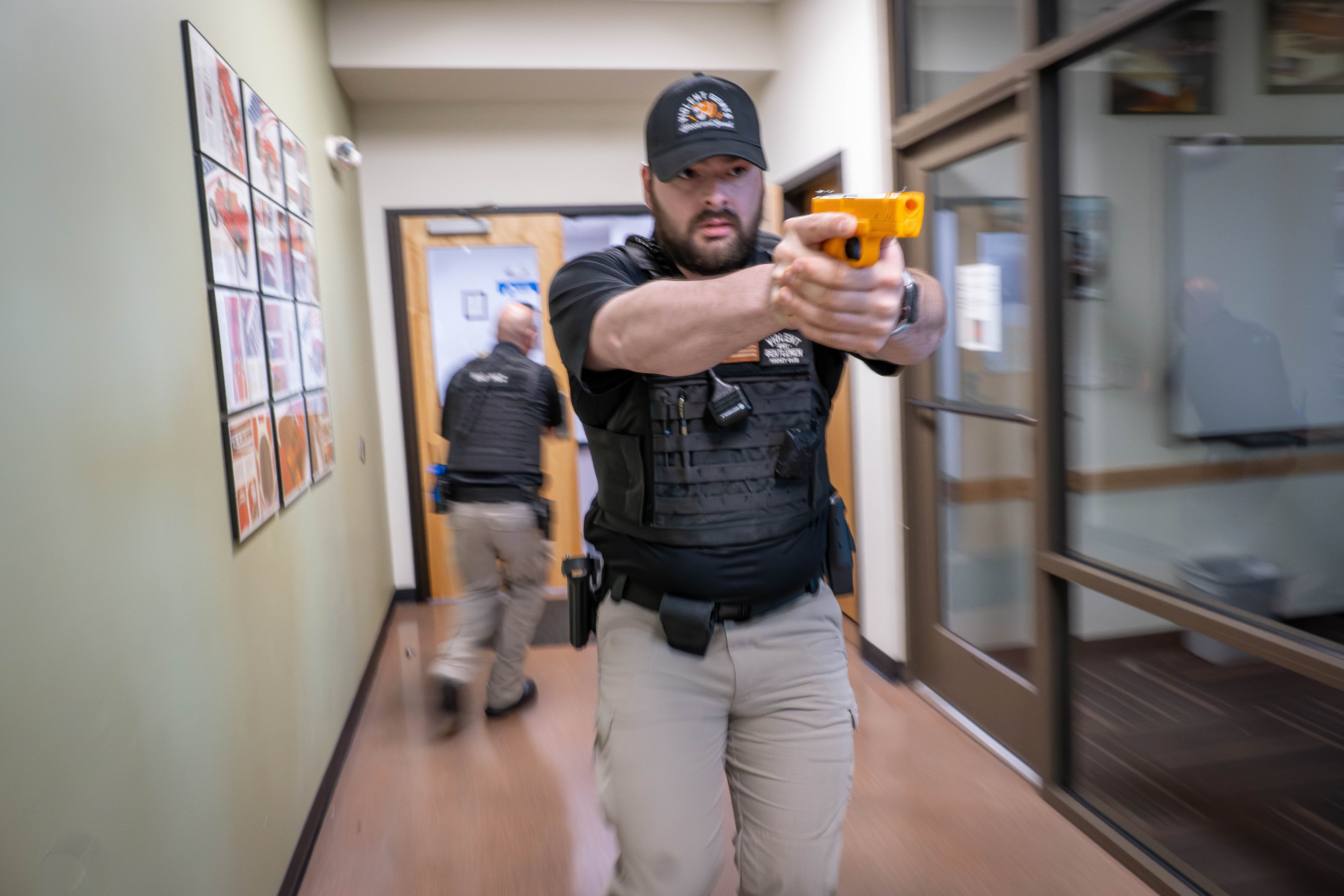 An Aims Peace Officer Academy cadet in action during an active shooter drill, in uniform holding a practice handgun