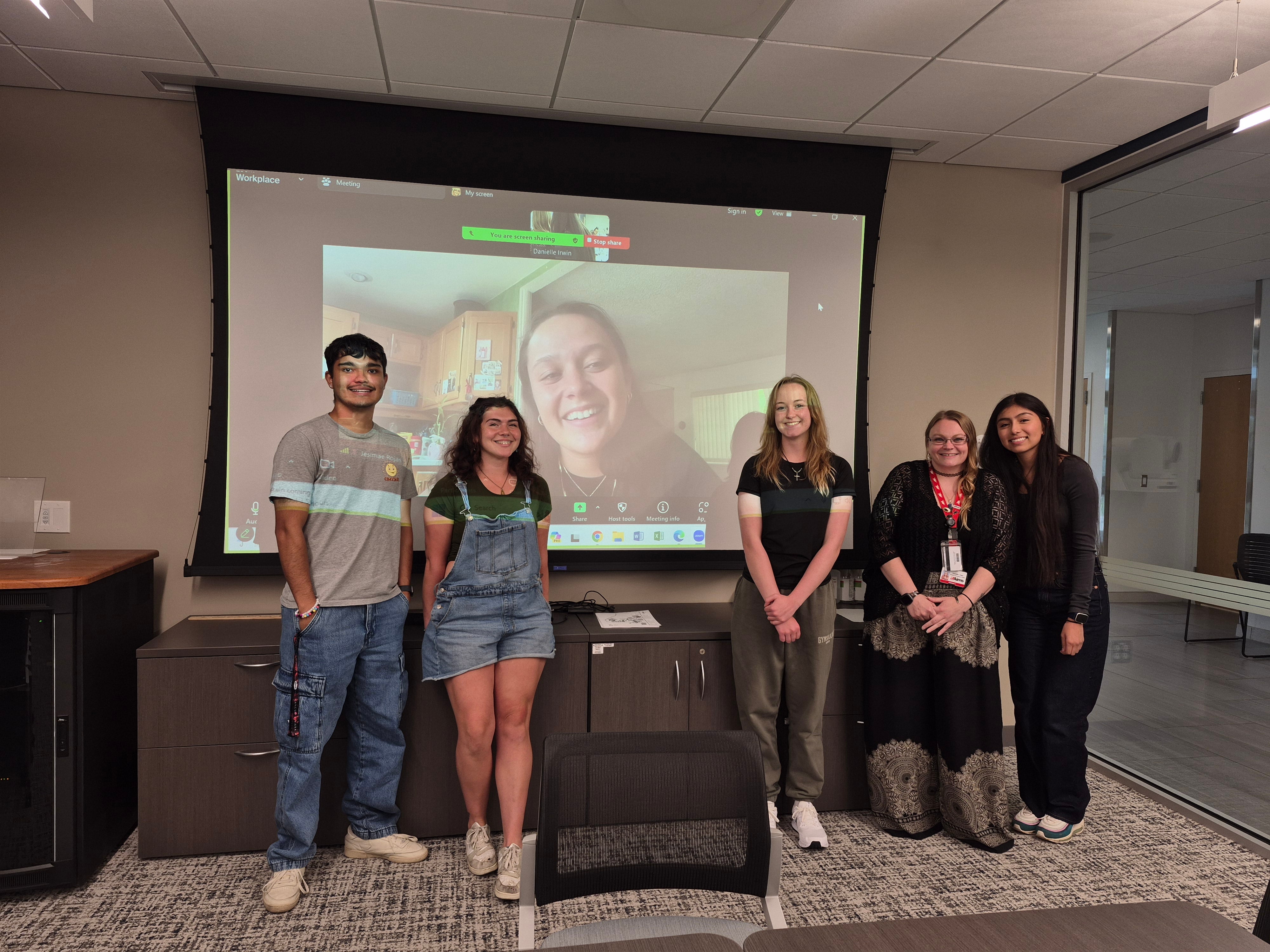 CAP students posing in front of a screen with a Zoom call showing another CAP student.