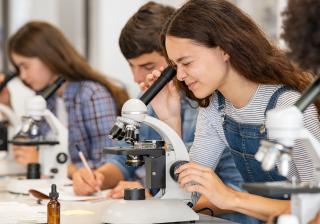 A group of biology students looking through microscopes in a lab class