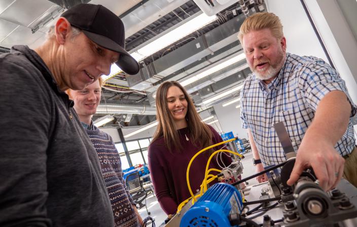 Aims students and a professor working with equipment in the industrial technology lab