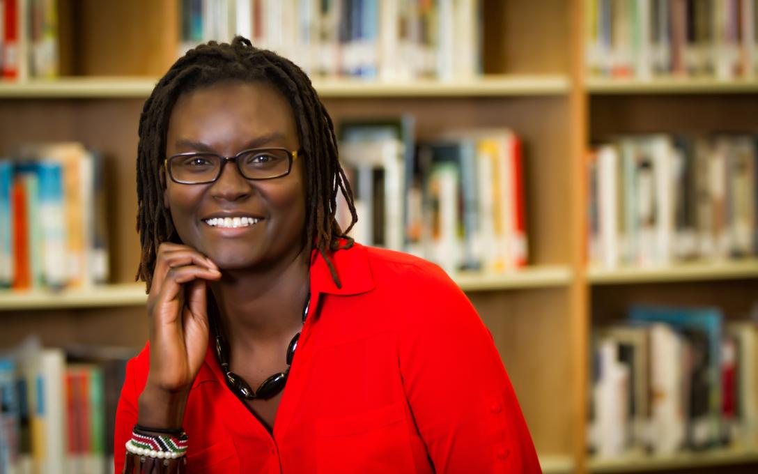 An Aims Community College Learning Commons staff member smiling in front of bookshelves