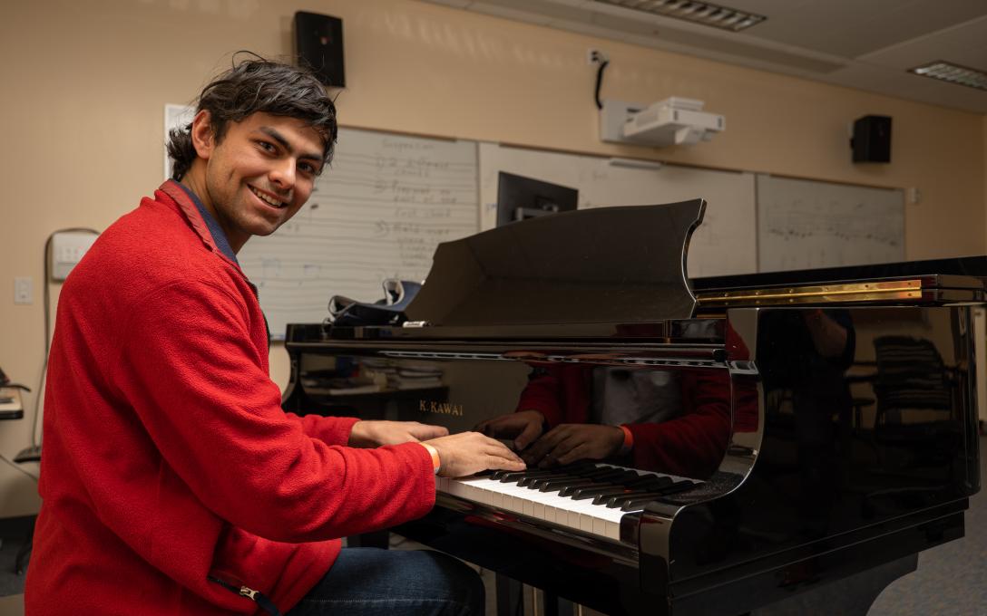 An Aims music student seated at a piano while smiling at the camera