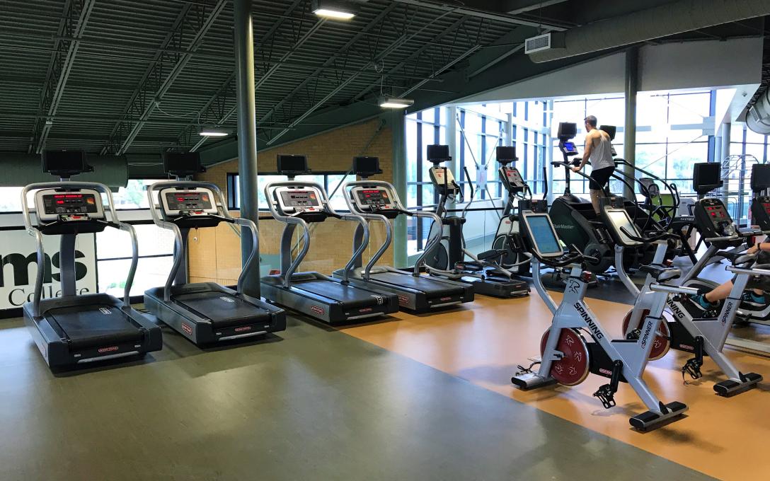 row of treadmills and ellipticals with man working out at the PERC