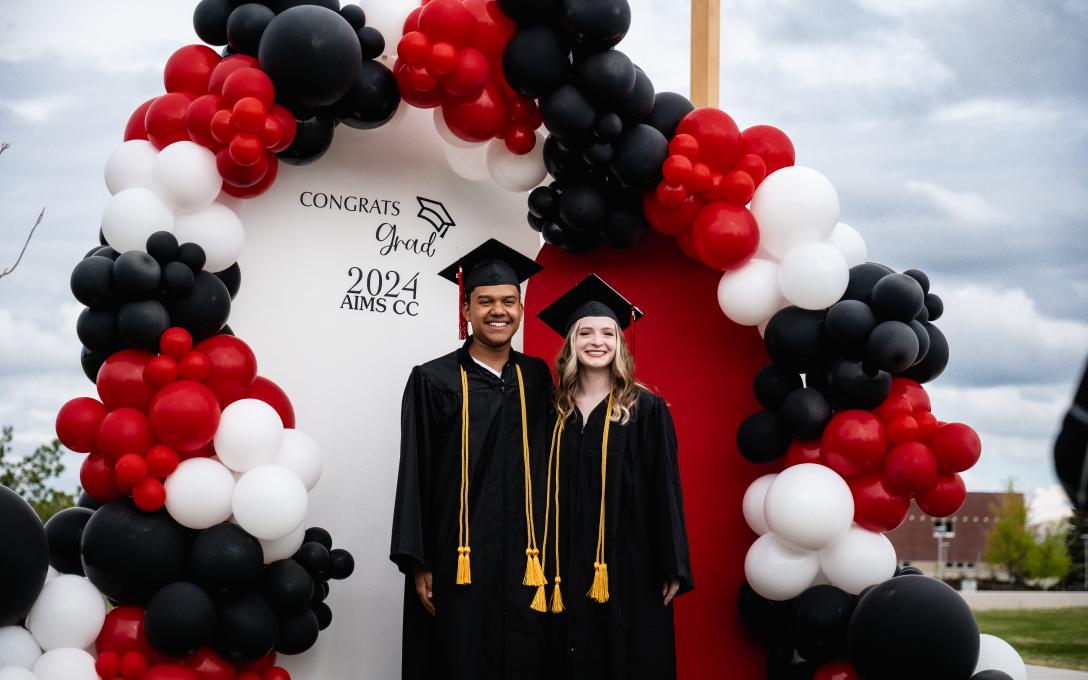 two grads posing with balloon display outside of welcome center