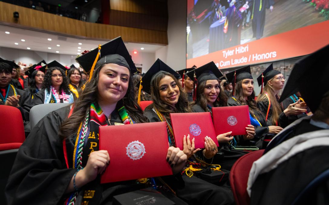 row of aims graduations holding their diplomas 