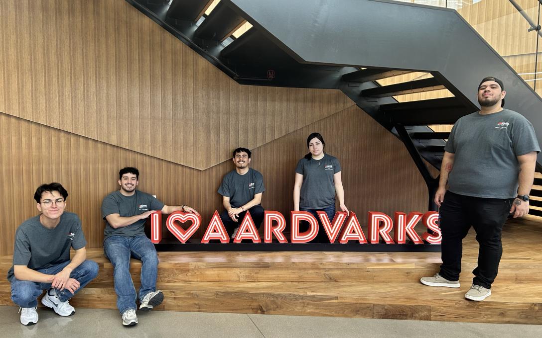 students standing in gray shirts, in front of I heart aardvarks sign
