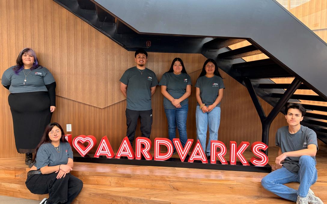 students standing in gray shirts, in front of I heart aardvarks sign