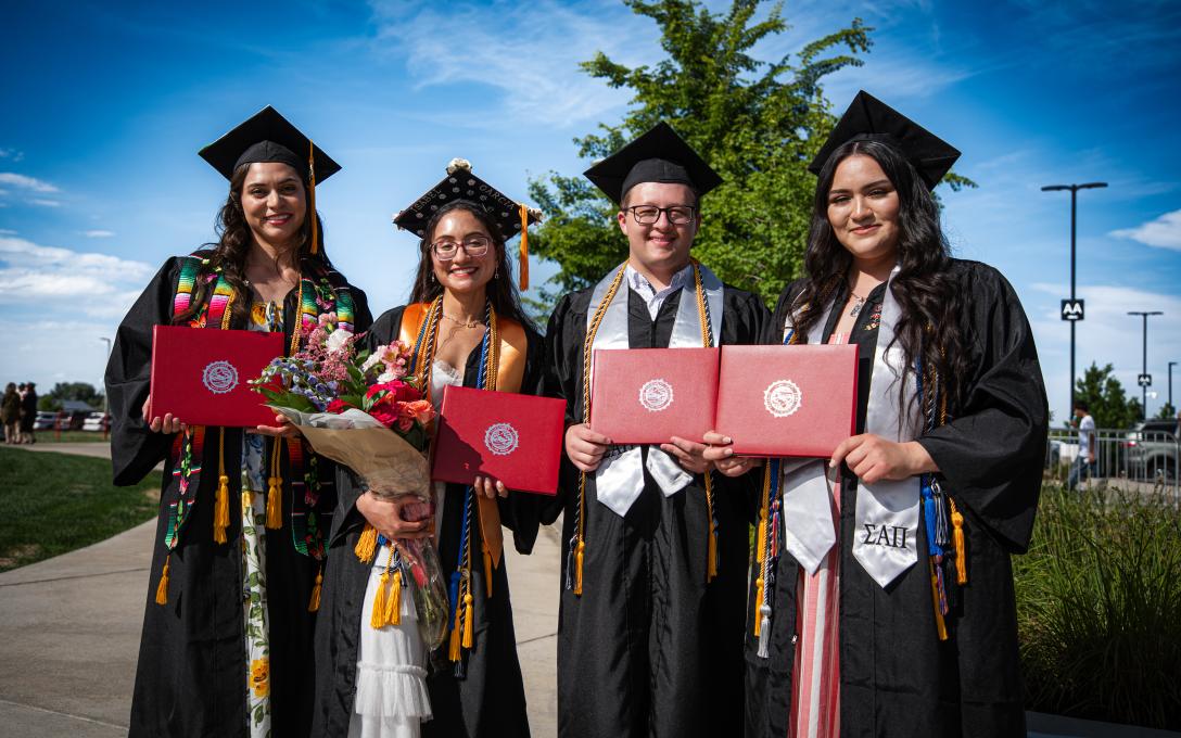 4 students with diplomas after graduation in caps and gowns