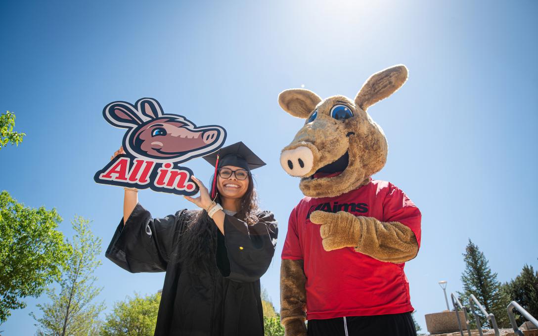 Arty and student in cap in gown with "All in" sign