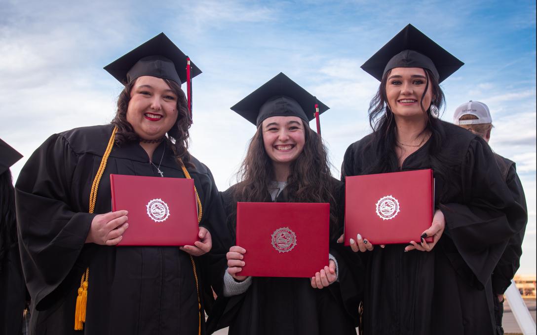 3 females in caps and gowns with diplomas
