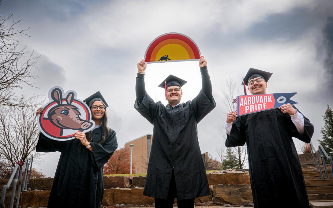 3 students in cap and gown with Aims signs