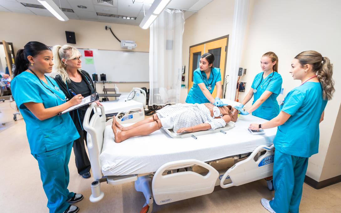 instructor and students standing around a hospital bed with mannequin patient
