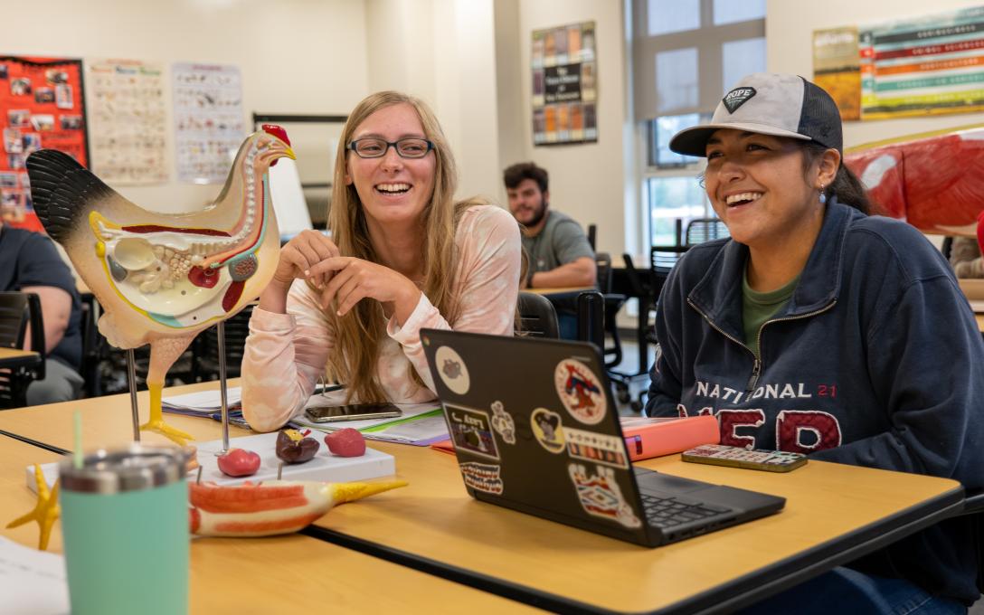 2 Aims ag students sitting in the ag classroom with laptop and a chicken anatomy model on the desktop