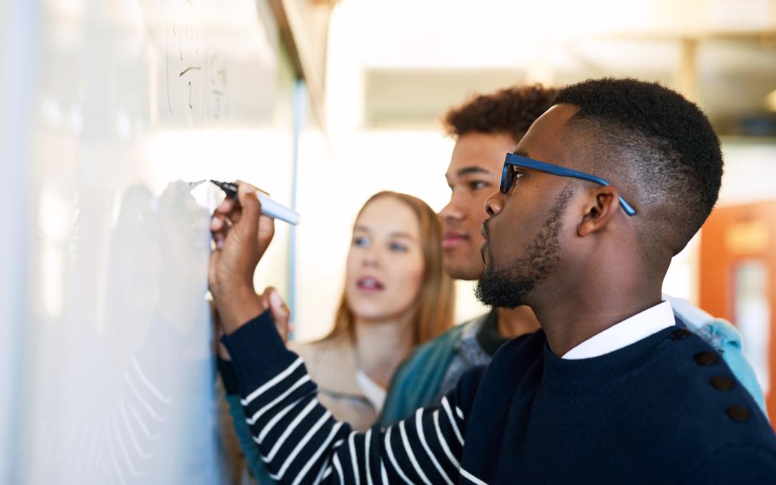 A group of students doing math problems at a whiteboard