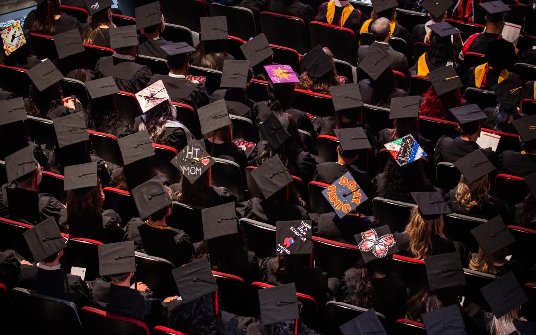 Dozens of Aims graduates sitting in the auditorium at commencement, photo shot from above showing the tops of their caps