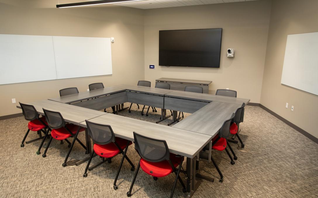 Room 249 conference room in the Aims Welcome Center showing tables set up in a square with chairs around outside and tv screen and white boards on the walls