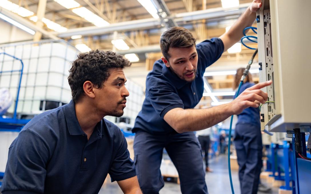two men wearing blue work clothes a shop looking at equipment