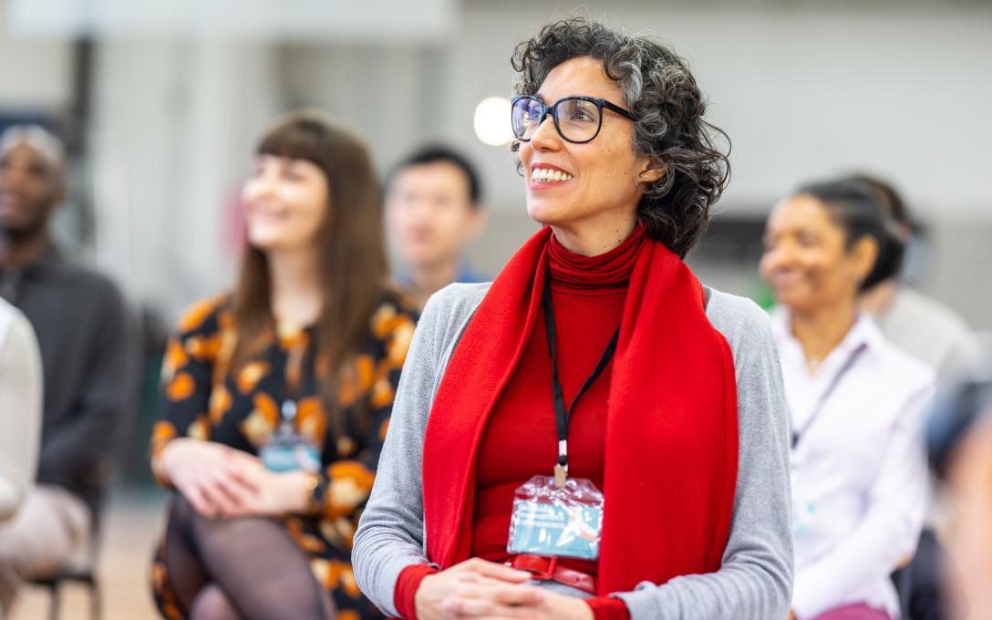 Woman seated wearing red shirt and glasses in front of four other people seated at a nonprofit leadership training event, all listening to presenter off camera