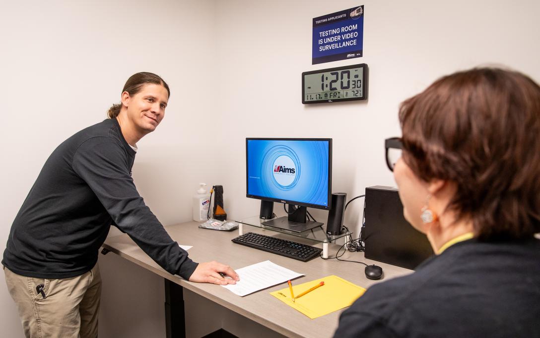 A testing center staff helps an Aims student prepare for a proctored test inside the Testing Center,
