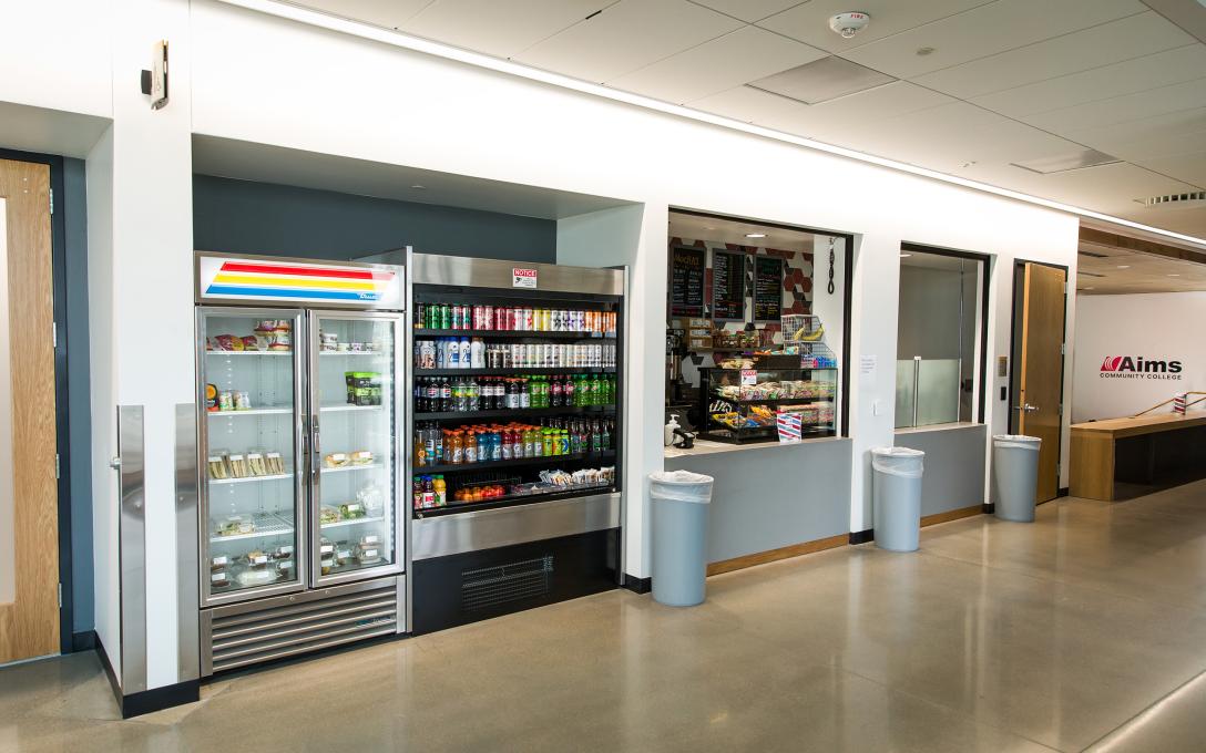 The storefront of Arty's Eatery, with a cooler for food and drinks, and a register to order fresh food.