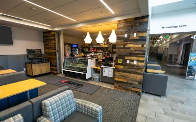 Exterior of Arty's Cafe. A cash register next to a cold food display with chairs and tables nearby.