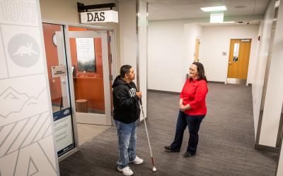 A student and staff member stand outside the entrance of the Disability Access Services office.