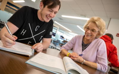 A student sits at a table with a tutor looking over a textbook