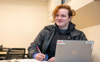 A student working at a desk with a pencil and a laptop