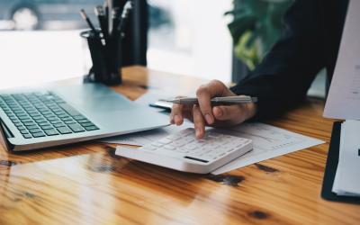 close up of hand making calculations on notepad with laptop open on a table