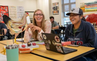 2 Aims ag students sitting in the ag classroom with laptop and a chicken anatomy model on the desktop