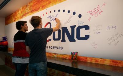 2 male Aims2UNC transfer students writing on the banner wall at transitions day