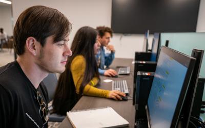 2 students sitting at a computer table each in front of a desktop computer, working