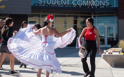 student in white dress twirling at dance dances with another student in black pants and red shirt outdoors as other students dance near them