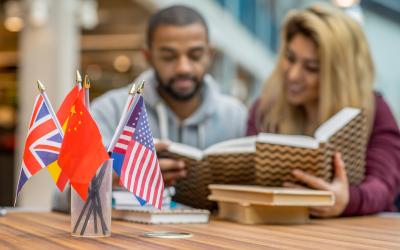 Two students sitting at a table reading language books with a jar with small international flags on the table in front of them