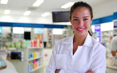pharmacy technician in white lab coat stands arms crossed at the front of pharmacy 