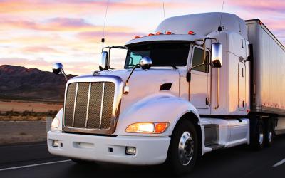 semi truck driving out of sunset with sky reflection on its side