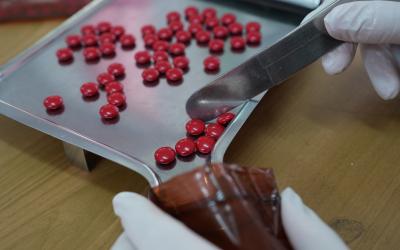 stainless steel tray with red pills, hand holding bottle and other hand scraping pills into bottle with metal tool