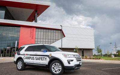 Aims campus security vehicle in front of the welcome center, white SUV with Aims logo and blue lettering that says Campus Safety and four campus names
